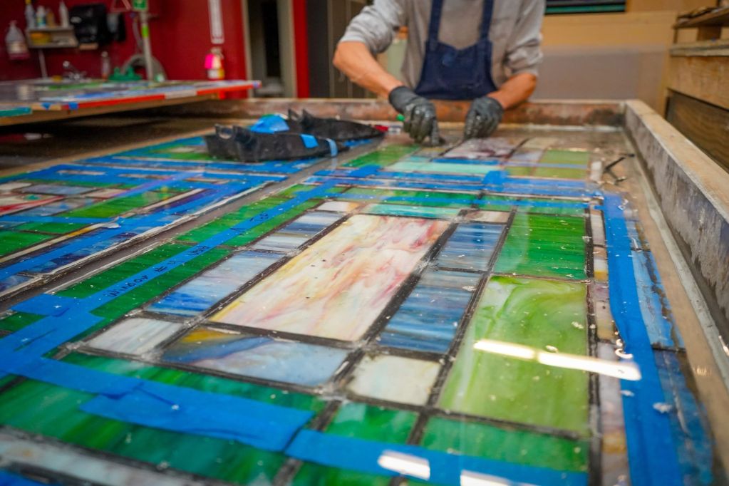 Artisan repairing stained glass window with blue tape and water, emphasizing stained glass restoration techniques and craftsmanship.