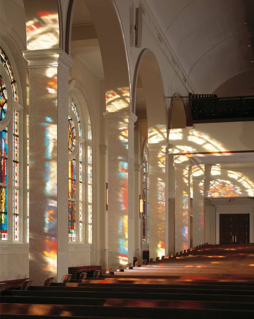 Stained glass windows illuminating a church interior, casting colorful reflections on polished surfaces, highlighting the architectural beauty and spiritual significance of the space.
