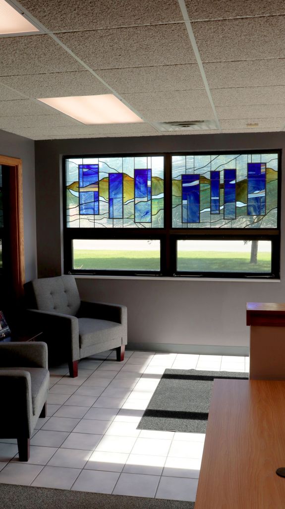 Architectural stained glass window featuring abstract blue and green designs, enhancing modern interior space with natural light, illustrating sustainable design elements in contemporary architecture.
