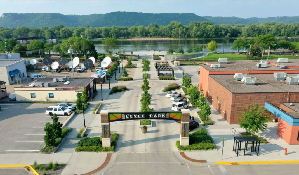 Levee Park entrance showcasing landscaped pathways, surrounding businesses, and river view, emphasizing community integration and outdoor aesthetics.