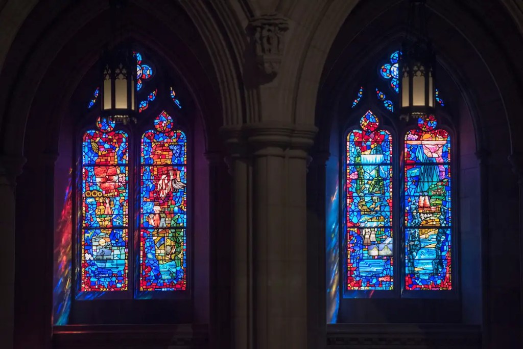 Stained glass windows depicting vibrant scenes of exploration and nature, showcasing the artistry of Willet Stained Glass Studios, enhancing the spiritual ambiance of a cathedral.