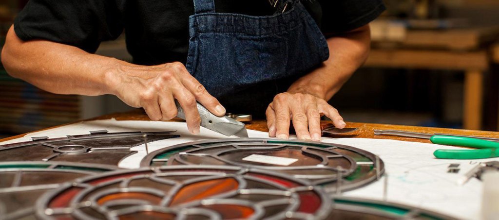 Craftsperson working on stained glass window design, showcasing intricate patterns and vibrant colors, reflecting the artistry of Willet Stained Glass Studios.