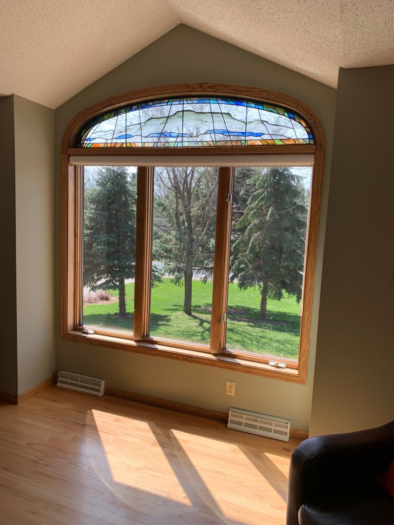 Stained glass window above a large bay window in a residential setting, showcasing vibrant colors and intricate designs, enhancing the interior space and natural light.