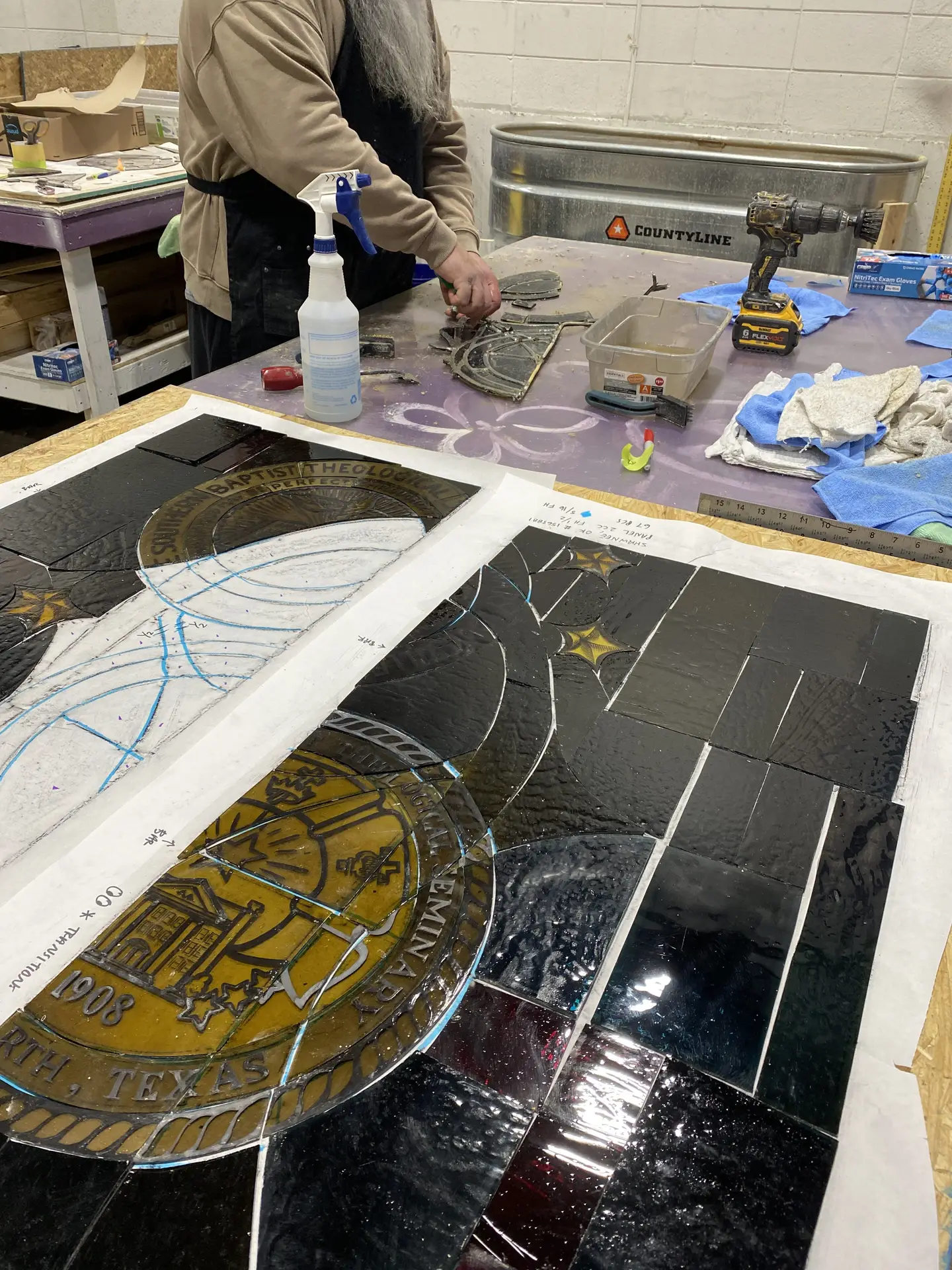 Artisan repairing stained glass panel with historical elements, tools and materials for restoration, workbench setting.