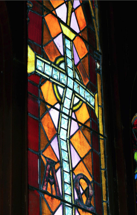 Stained glass window featuring a central cross design with vibrant orange and purple hues, illustrating the artistry and condition of stained glass in need of assessment for conservation.
