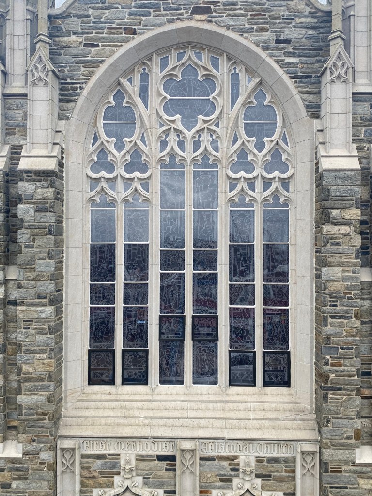 Gothic-style stained glass window in a church, showcasing intricate designs and stone architecture, emphasizing protective coverings for heritage preservation.