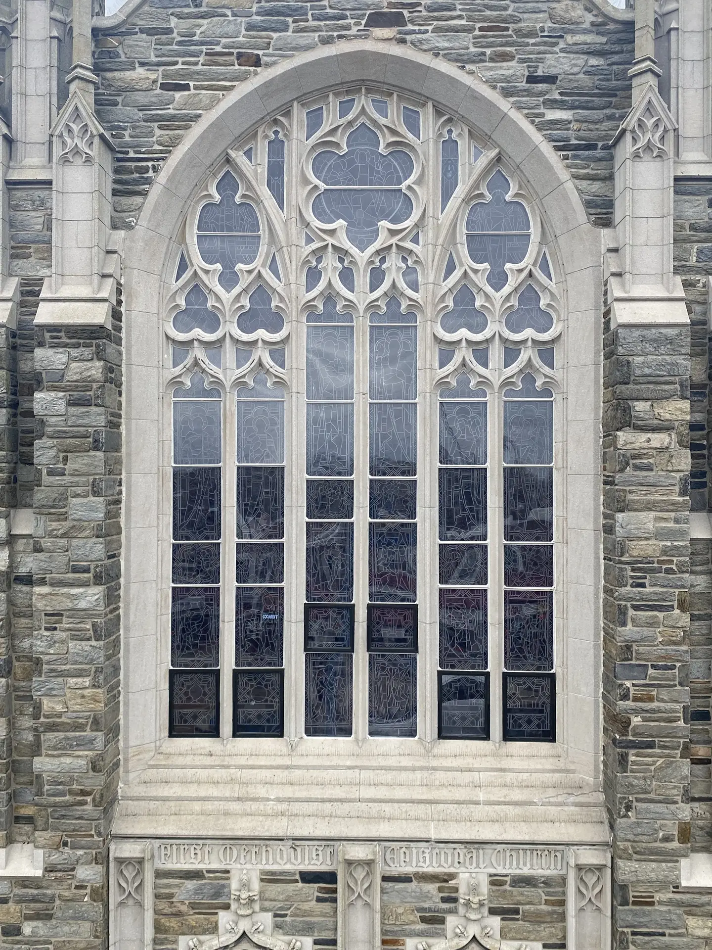 Gothic-style stained glass window with protective glazing, showcasing intricate designs and stone architecture of a historic church.