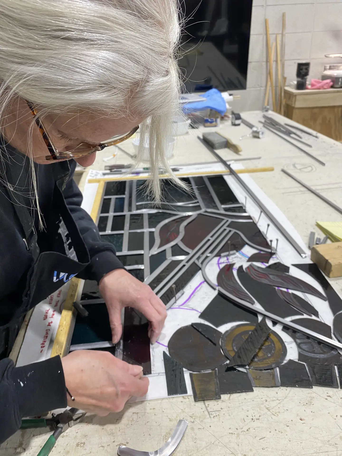 Artisan assembling stained glass pieces using the lead came technique, showcasing intricate patterns and craftsmanship in a studio setting.