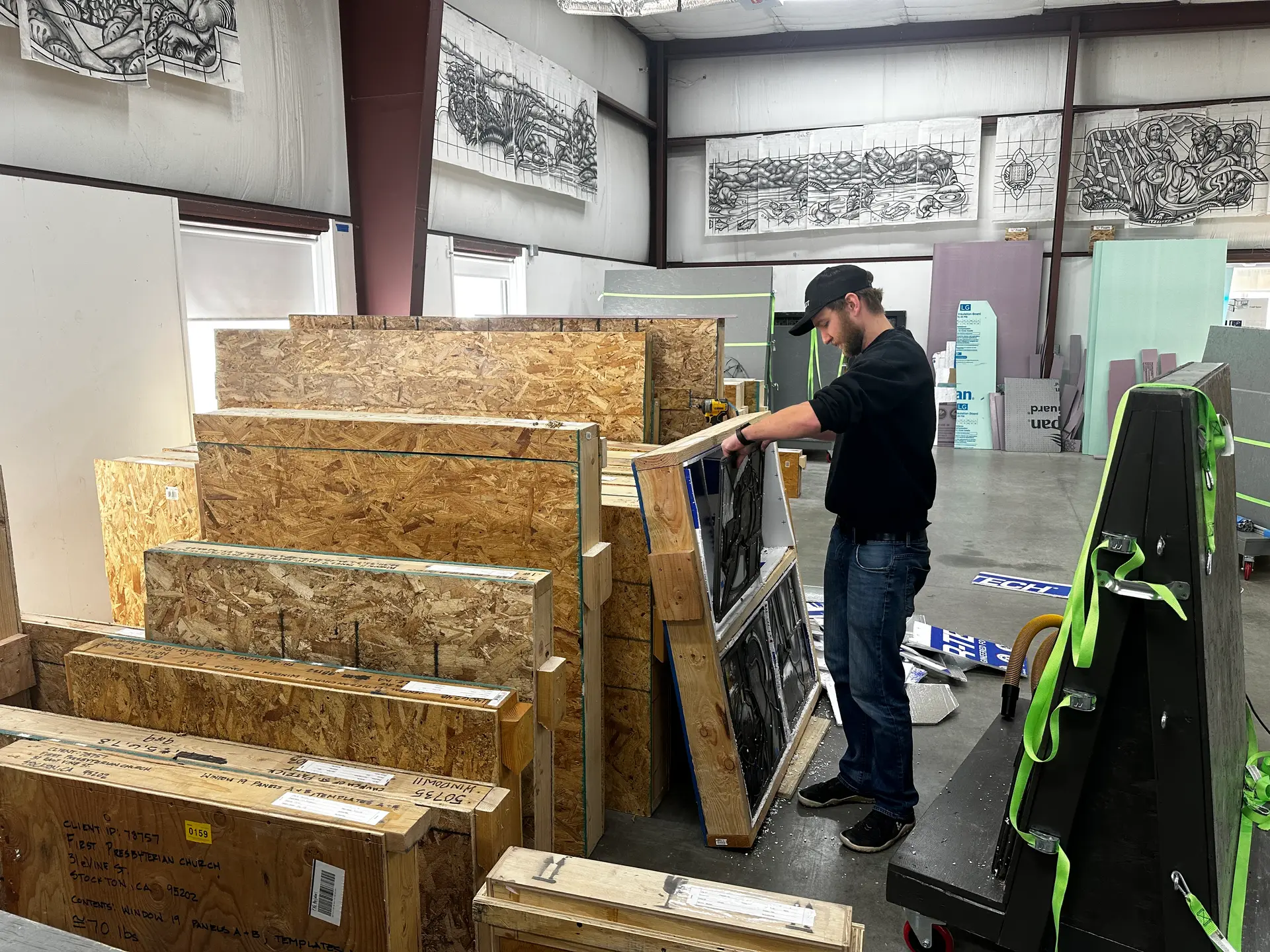 Worker preparing stained glass panels for restoration, surrounded by protective crates and materials in a studio setting.