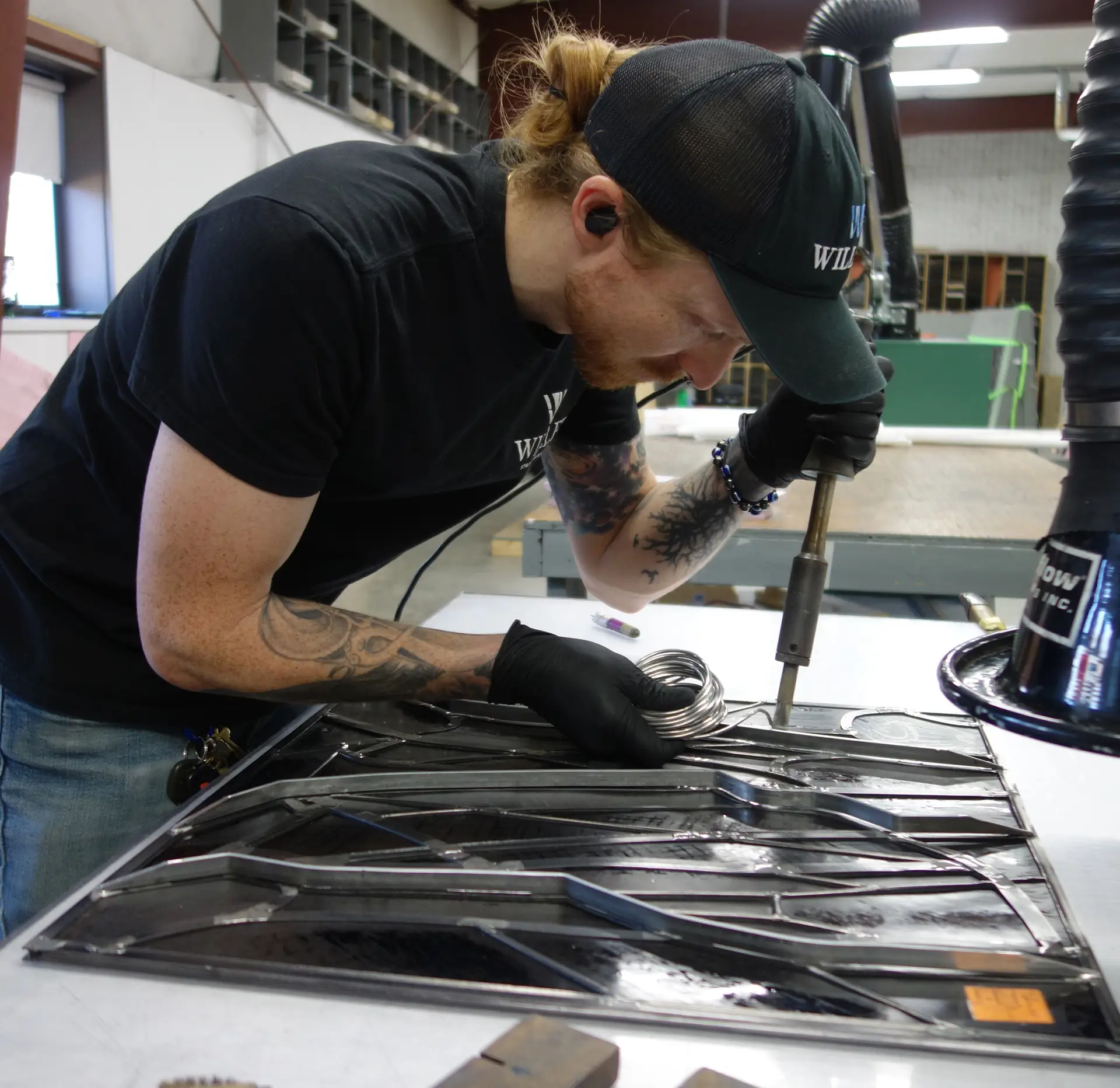 Technician working on stained glass restoration, using a soldering tool and wearing gloves, showcasing craftsmanship at Willet Stained Glass Studios.
