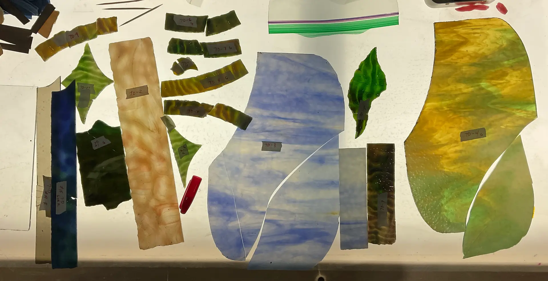 Assorted stained glass pieces with labels, showcasing various colors and textures, used for condition assessments and restoration planning.