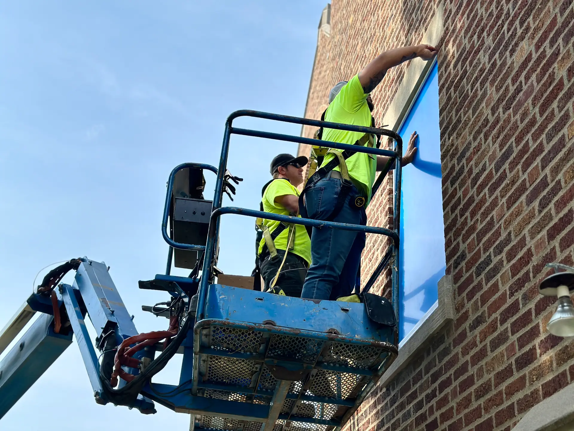 Construction workers installing protective glazing on brick building exterior.